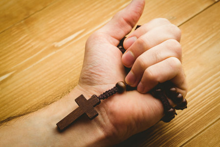 Close-up of hand holding rosary beads against wooden tableの写真素材