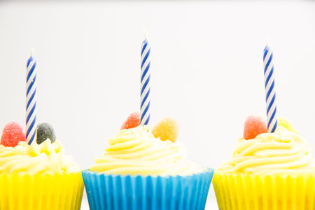 vector art showing three yellow-frosted cupcakes blue striped candles, gumdrops on white background....