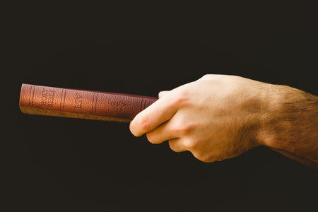 Close-up of hand holding Bible over black background