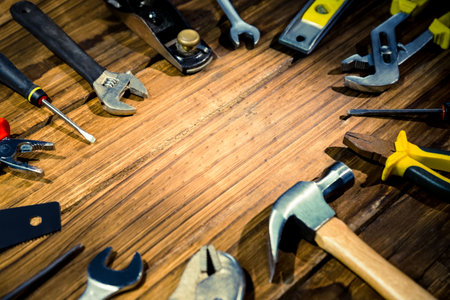 Hammer, wrenches, pliers and screwdrivers are lying flat around warm wood workbench in flat design....