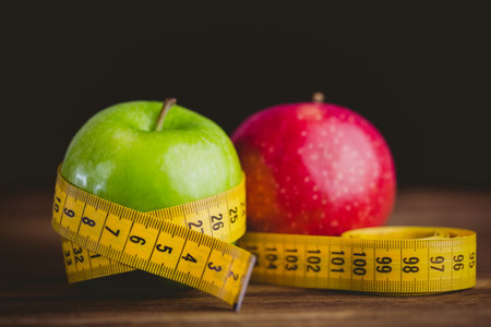 Red and green apples with measuring tape on wooden tableの写真素材