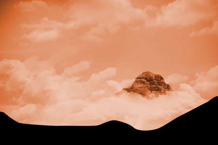 Rocky mountain peak is emerging through orange-tinted cloud layers over abstract black silhouette. Mountain, landscape, abstract, rugged, atmospheric, elevation, twilightの写真素材
