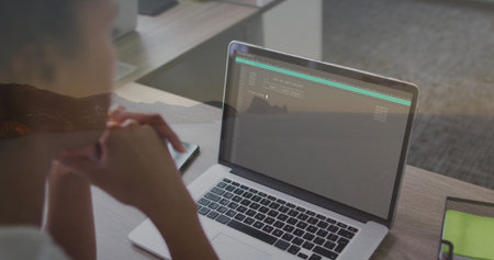 Leaning woman viewing laptop terminal in office, with smartphone and green mesh pouch, copy space....