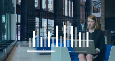 Woman in blazer typing on laptop on blue sofa in office lounge, bar-chart overlay, copy space. Modern, professional, collaborative, contemporary, architecture, workspace, communicationの写真素材