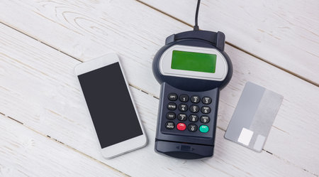 Payment devices are showing on white table, flat design featuring smartphone, reader, credit card. Technology, commerce, retail, minimalism, digital, transaction, financialの写真素材