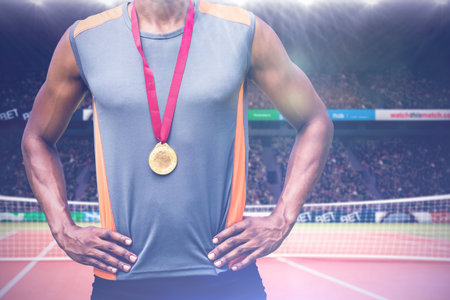 Portrait of male athlete standing with hands on hip and medals at stadiumの写真素材