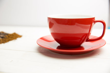 Flat design is showing red ceramic cup and saucer resting on wooden tabletop with scattered grounds. Minimalist, rustic, cozy, warm, kitchen, cafe, craftsmanshipの写真素材