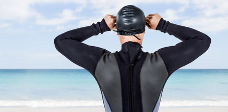 Rear view of male swimmer adjusting swimming cap while standing at beachの写真素材