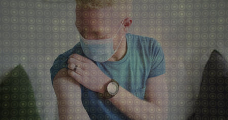 Man wearing protective face mask pulling up shirt sleeve and touching arm at home, with wristwatch. Health, safety, wellness, relaxation, comfort, casual, modernの写真素材