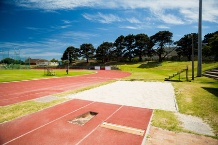 Long jump runway and sandpit are stretching across grassy field in flat design, showing red track. Athletics, sport, outdoor, competition, endurance, equipment, trainingの写真素材
