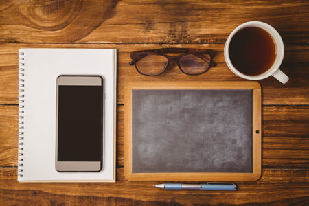 Showing flat-design overhead desk with pad and smartphone, framed chalkboard, glasses, coffee, pen. Stationery, workspace, minimalism, productivity, interior, innovation, focusの写真素材