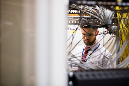 IT technician is examining network cables with handheld device in flat design server rack scene....