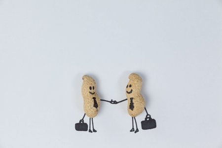 Smiling peanut figurine business people shaking hands against paperの写真素材