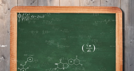 Leaning green wood-framed chalkboard in study showing chemical and physics formulas on plank wall....