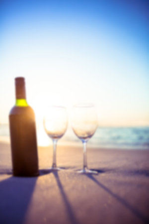 Flat design wine bottle and two glasses are resting on sandy shoreline, casting long shadows. Beach, relaxation, serenity, summer, leisure, elegance, outdoorsの写真素材