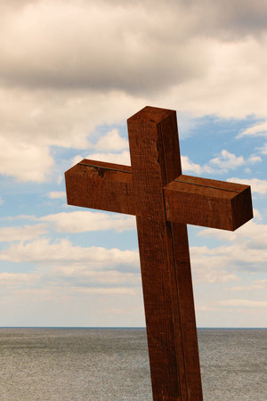 weathered wooden cross is standing before calm sea horizon under cloudy sky in flat design style....