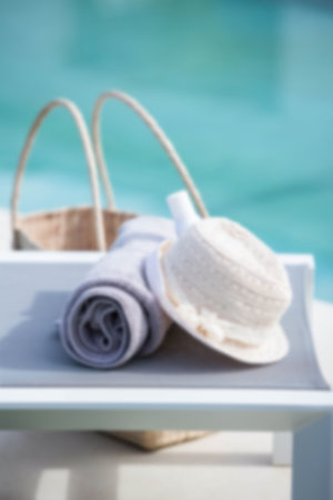 Towel and hat on table against swimming poolの写真素材