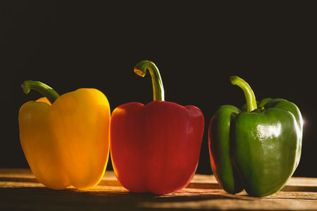 Close-up multi colored bell peppers arranged in a row over black backgroundの写真素材