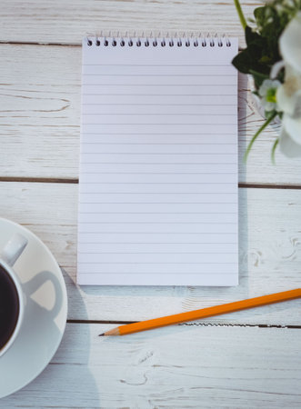 Close-up of spiral book with pencil between coffee cup and flower pot on tableの写真素材