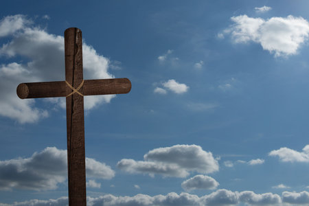 Rustic wooden cross is standing against bright blue sky with scattered white clouds, flat design. Spiritual, faith, tradition, symbol, serenity, natural, minimalistの写真素材