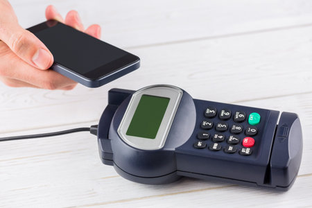 Contactless payment processing with smartphone and POS terminal in flat design on wooden countertop....