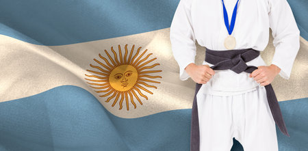 Midsection male martial artist tying belt against Argentinian Flagの写真素材