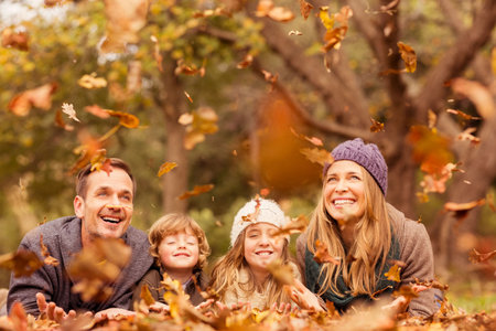 Happy family playing with leaves at park during autumn