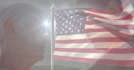 Showing mature couple facing each other outdoors, with waving American flagpole and sun lens flare. Patriotism, freedom, unity, outdoor, sunlight, perseverance, generationalの写真素材