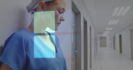 Leaning worker wearing scrubs and cap monitoring interface squares in hospital corridor, copy space....