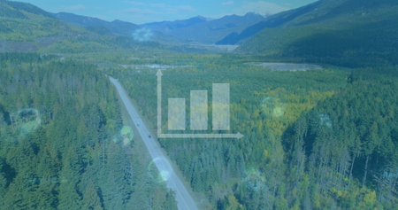 Snaking paved highway winding through conifer forest in mountain valley, with two cars and peaks....