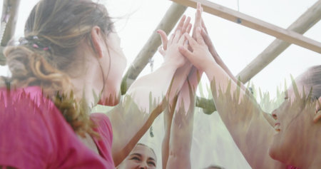 Stretching women raising arms and touching palms under monkey bars, wearing pink shirts and earbud....