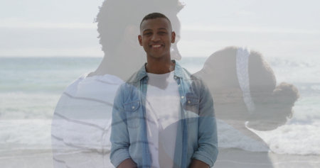 Smiling man standing at sandy beach edge, with ocean waves and embracing couple silhouette....