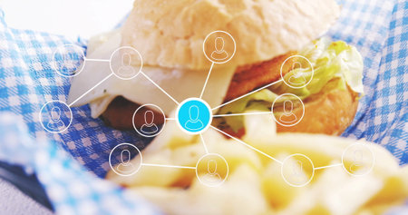 Showing burger sandwich resting on checkered liner in cafe, with cheese, fries and network graphic....