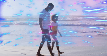 Walking father and son strolling along wet sand at beach edge, wearing striped and color-block tops. Family, outdoor, relaxed, vibrant, lifestyle, leisure, scenicの写真素材