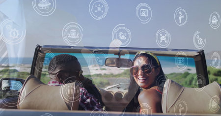 Smiling couple turning heads toward camera in cream convertible on coastal road, tech icons....