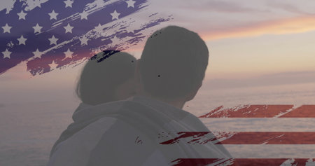 Embracing couple watching ocean horizon at sunset, with translucent US flag overlay. Romantic, serenity, natural, tranquility, connection, dawn, silhouetteの写真素材