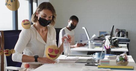 Office worker spraying and wiping desk at open-plan workspace, with spray bottle and cloth. Collaboration, hygiene, productivity, modern, professional, clean, workspaceの写真素材