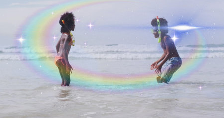 Playing children wearing swimwear yellow vest snorkel gear in shallow beach water under rainbow arc. Adventure, outdoor, vibrant, playful, exploration, leisure, scenicの写真素材