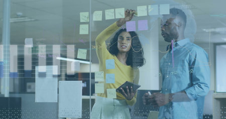 Placing sticky note, brainstorming plan in business attire on glass board in office, with tablet....