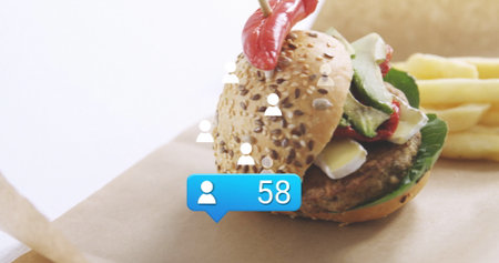 Displaying seeded burger with greens, cheese and fries on table featuring user icons and 58 bubble. Gourmet, healthy, vibrant, contemporary, digital interaction, casual dining, fresh ingredientsの写真素材