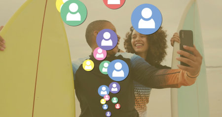 Leaning hugging friends taking smartphone selfie on beach at sunset with surfboards, floating icons. Friendship, leisure, coastal, vibrant, social, carefree, harmonyの写真素材