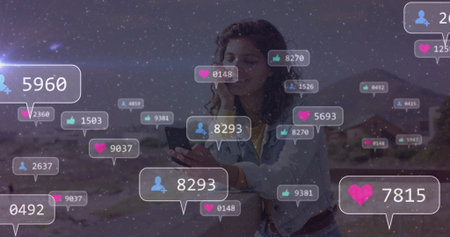 Holding smartphone, woman wearing denim jacket engaging with floating social icons in desert canyon....