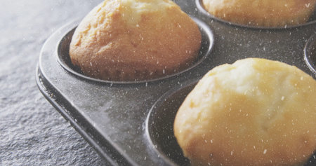 Displaying close-up metal muffin tin holding golden-brown muffins on dark kitchen countertop....