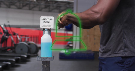 Man in grey shirt and shorts sanitising hands using pedal sanitiser station inside gym, copy space....