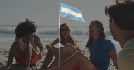 Four friends chatting in swimwear at sandy beach water's edge, with blue white flag and sunglasses. Beach, leisure, relaxation, summer, outdoor, social, vibrantの写真素材