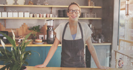Standing woman wearing striped apron working behind wooden counter at coffee shop, with grinder....