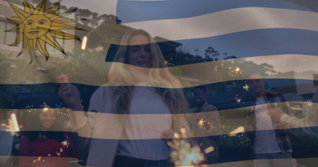 Holding sparklers, group of six adults celebrating in backyard at dusk, with Uruguayan flag overlay. Festivity, camaraderie, outdoor, dusk, illumination, multicultural, unityの写真素材