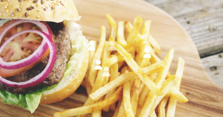 Displaying hamburger resting on wooden board with lettuce tomato red onion and seasoned fries....