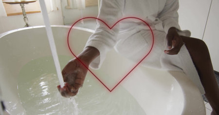Woman in white bathrobe directing hand under faucet into bathtub in bathroom, with heart outline. Relaxation, selfcare, wellness, tranquility, minimalism, natural light, home spaの写真素材