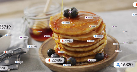 Amber syrup drizzling over brown pancake stack on plate at kitchen table, with blueberries, alerts....